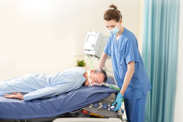 A healthcare staff takes care a critical patient laying down (Prone) with Optima Prone (Support Surface)